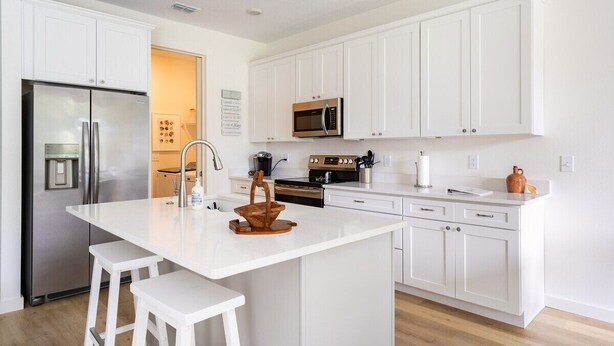 A modern kitchen with white cabinetry, a stainless steel refrigerator, a microwave, and a central island with stools.
