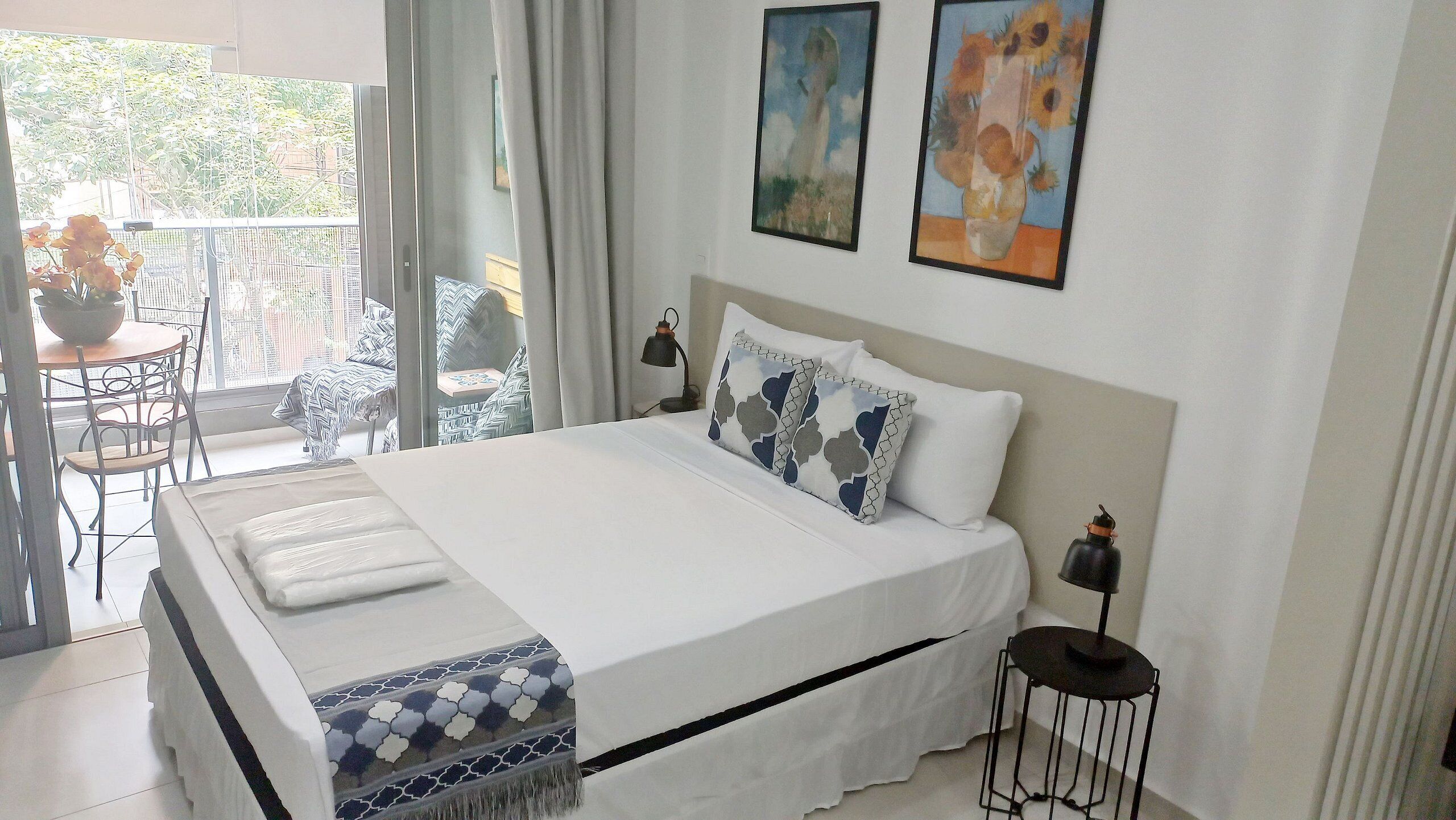 Une chambre à coucher avec un lit, des oreillers, une table de chevet, une lampe et une vue sur le balcon extérieur.