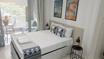 Une chambre à coucher avec un lit, des oreillers, une table de chevet, une lampe et une vue sur le balcon extérieur.