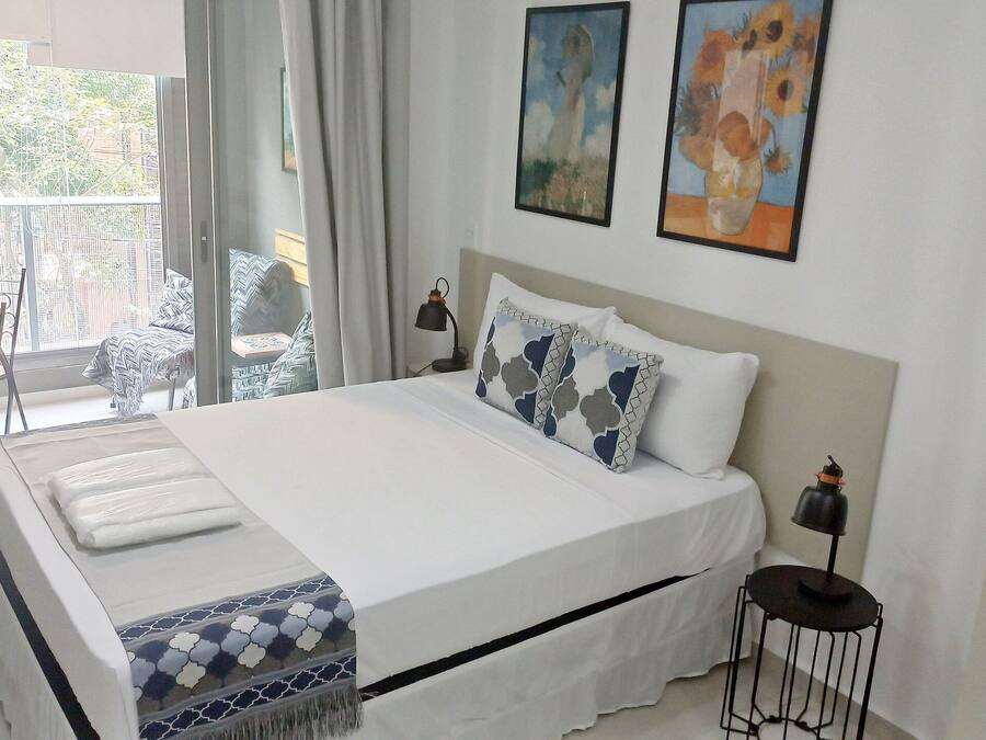 Une chambre à coucher avec un lit, des oreillers, une table de chevet, une lampe et une vue sur le balcon extérieur.