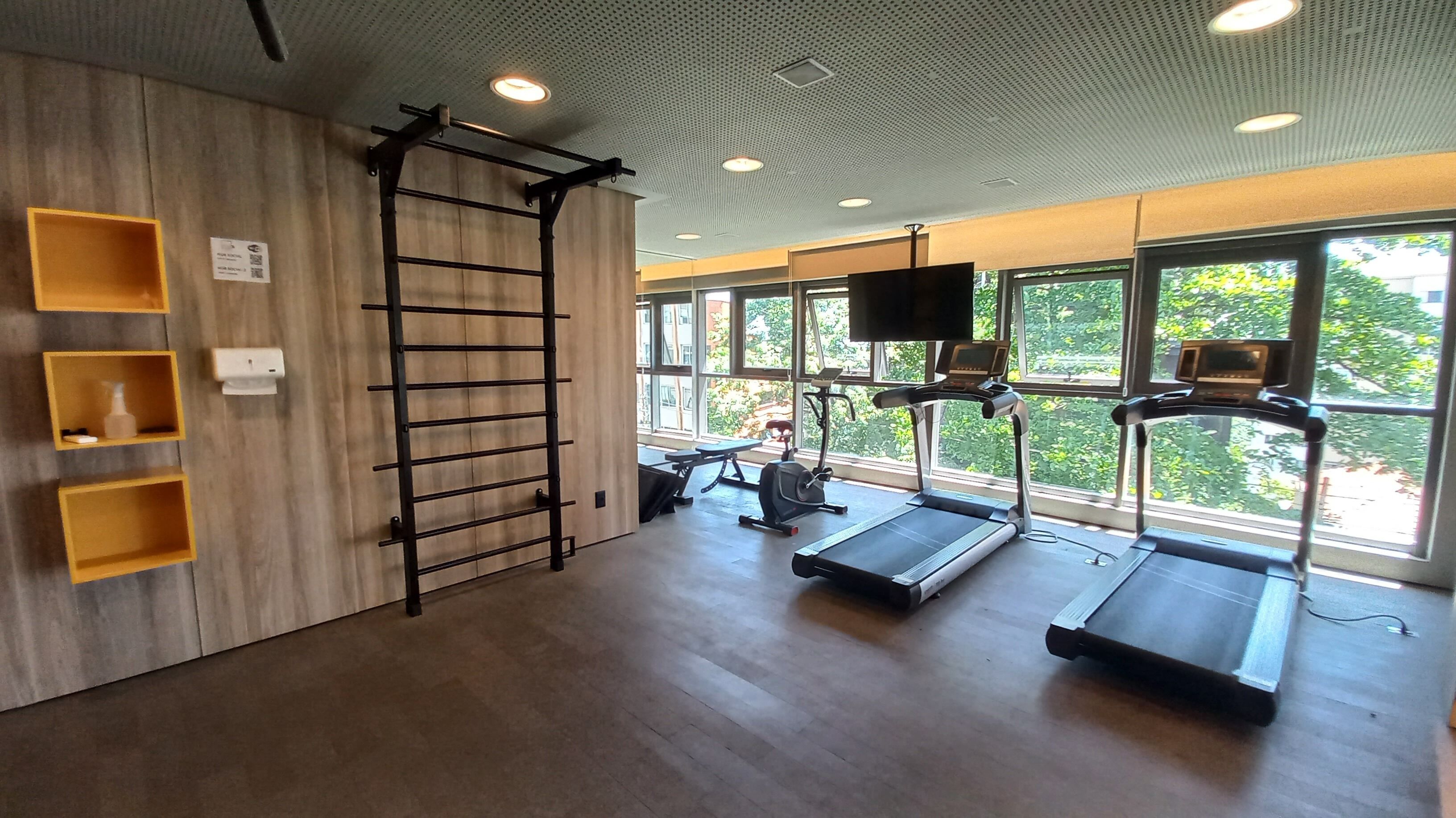 Un gimnasio con piso de madera, barra de dominadas, cintas de correr y una pantalla de televisión.