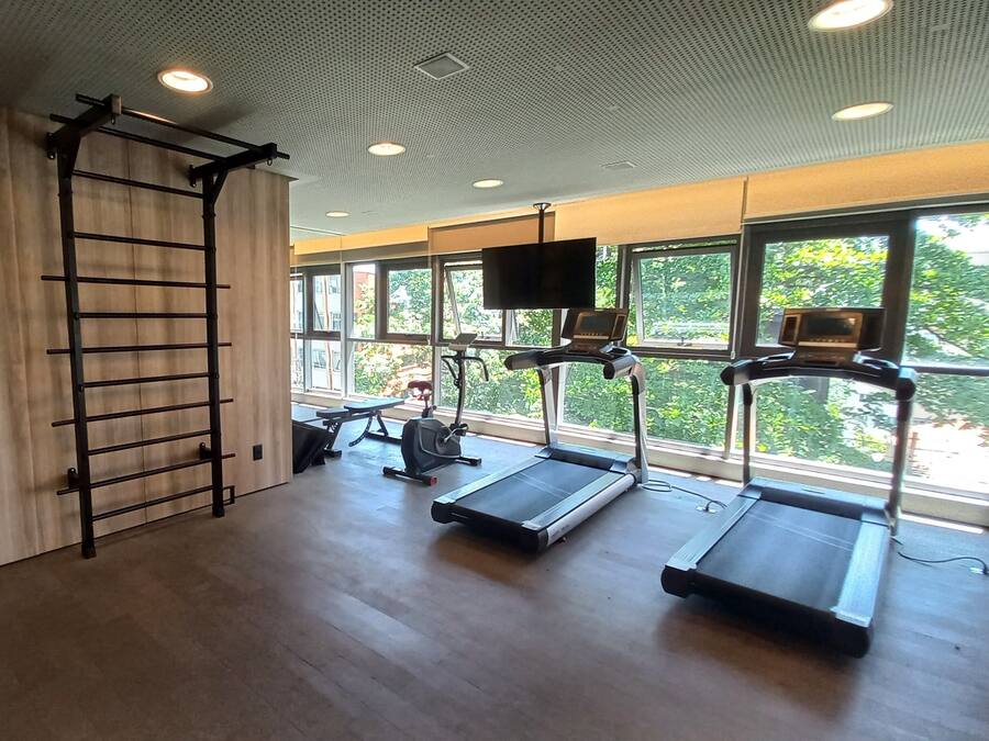 Un gimnasio con piso de madera, barra de dominadas, cintas de correr y una pantalla de televisión.