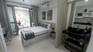 Een kleine hotelkamer met een bed, een nachtkastje, een spiegel en een kitchenette.