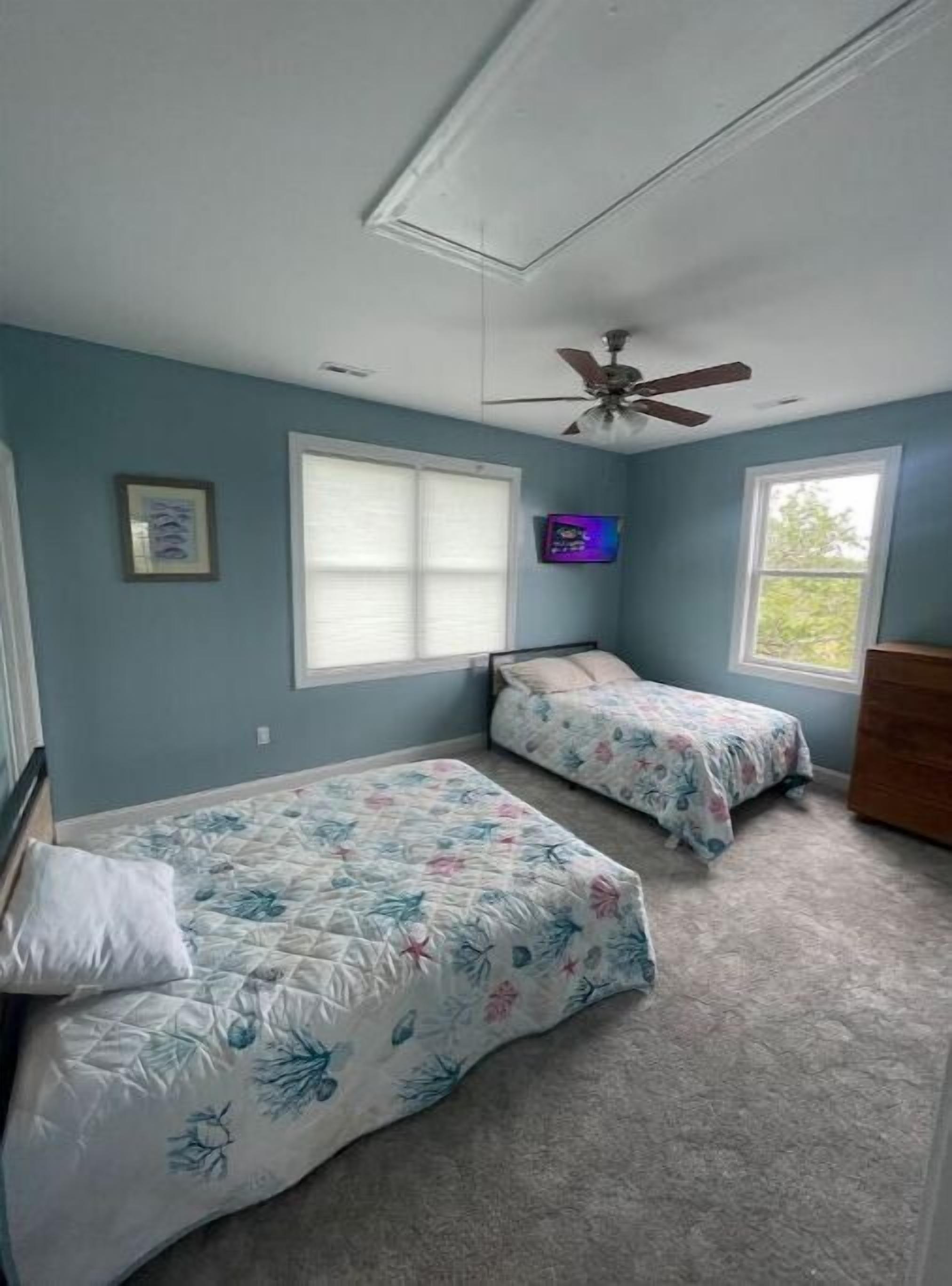 A bedroom with two beds, a ceiling fan, and a window with blinds.