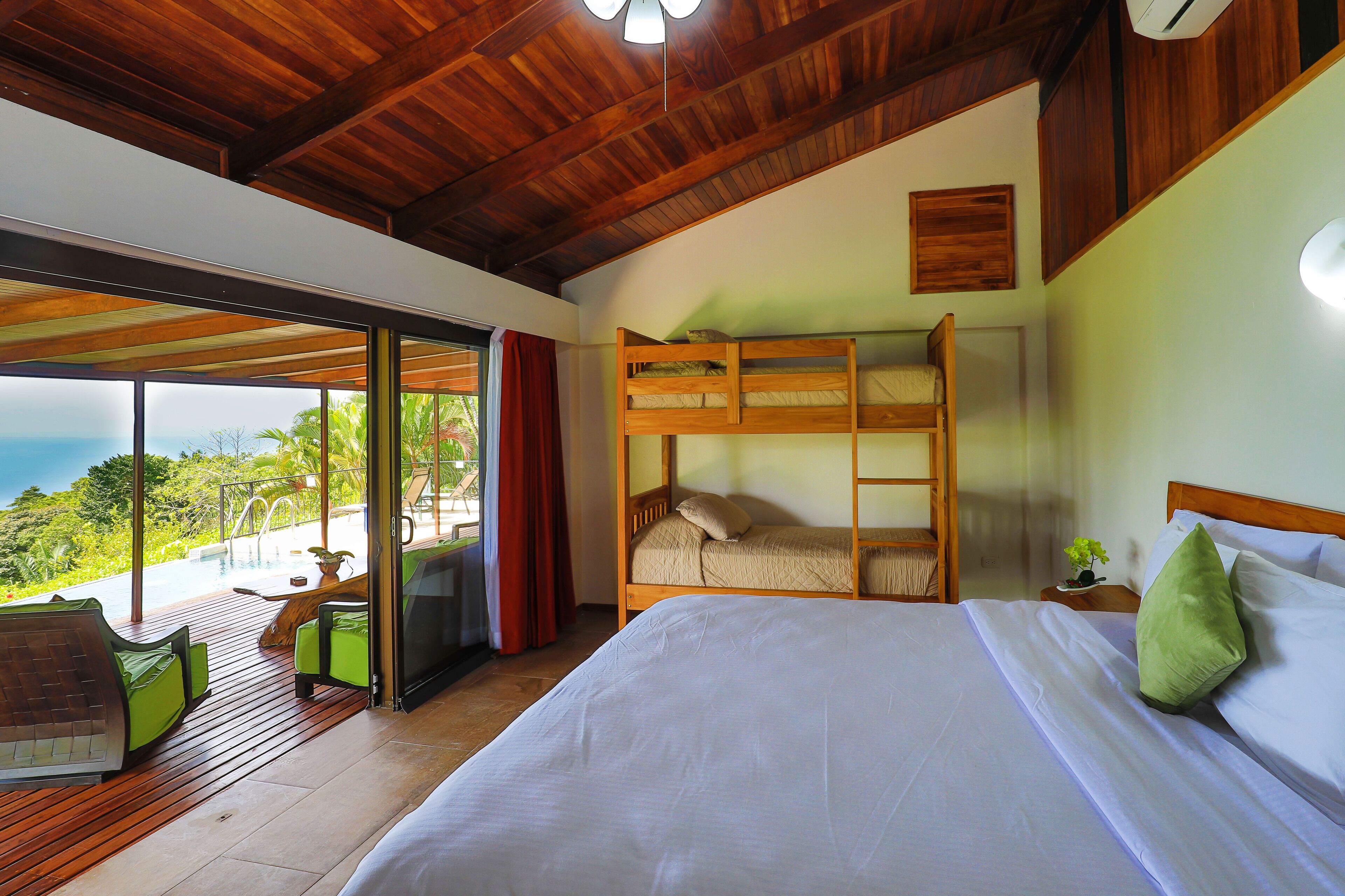 A bedroom with a large bed, a wooden bunk bed, and a view of the ocean through a sliding glass door.