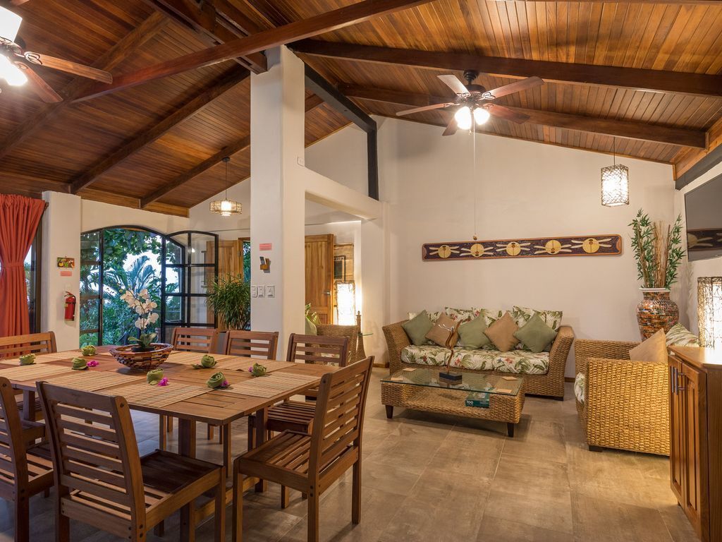A spacious living area with a wooden ceiling, a dining table with chairs, a sofa, and a coffee table.