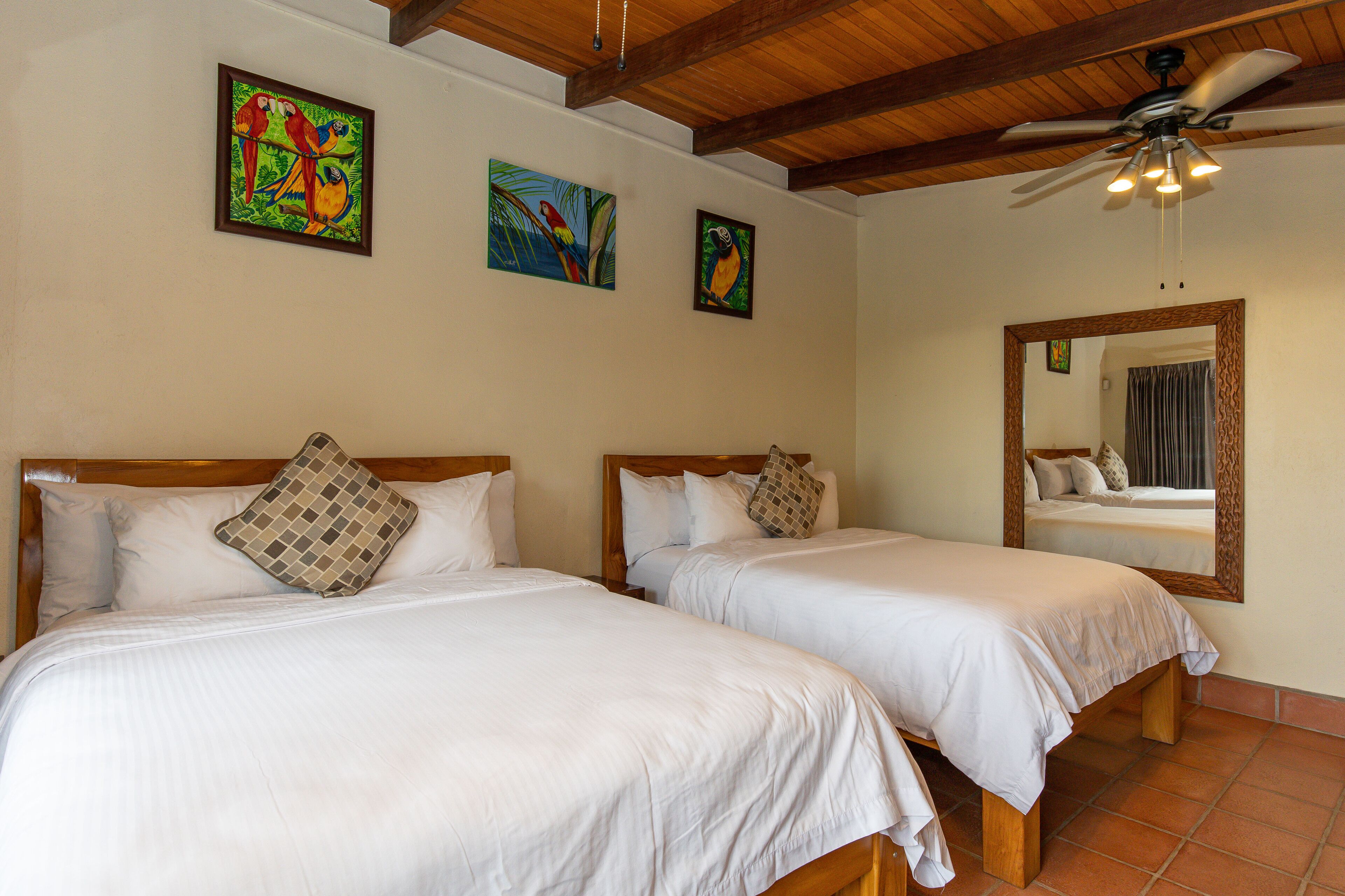 A hotel room with two beds, wooden headboards, white bedding, and a ceiling fan.