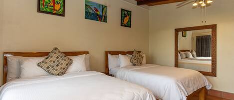 A hotel room with two beds, wooden headboards, white bedding, and a ceiling fan.