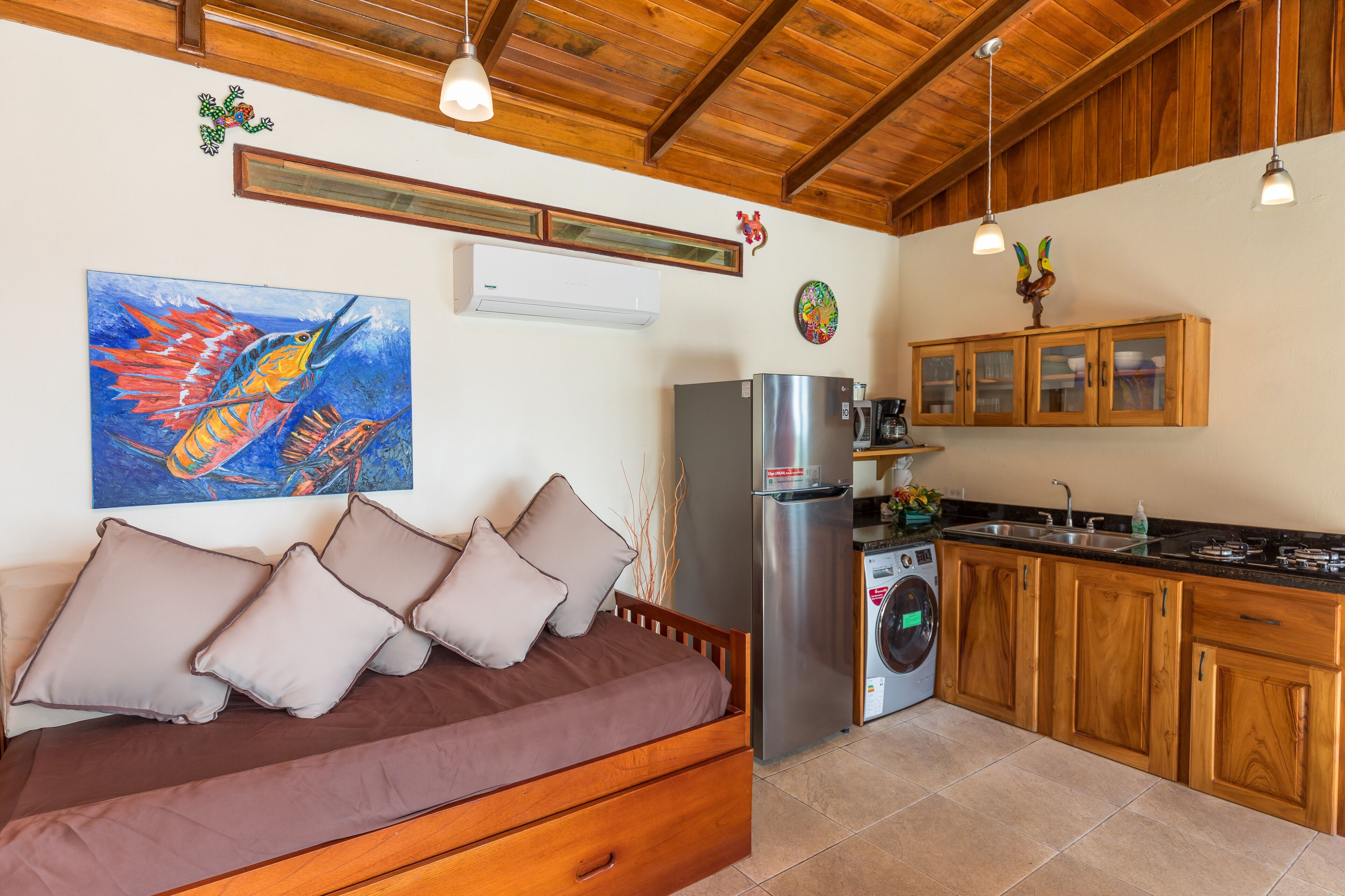 Una habitación compacta con cama, lavadora, refrigerador, armarios de madera y un cuadro en la pared.