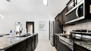Une cuisine moderne avec des meubles de couleur sombre, des comptoirs en granit, des appareils électroménagers en acier inoxydable et un dosseret orné de carreaux à motifs.
