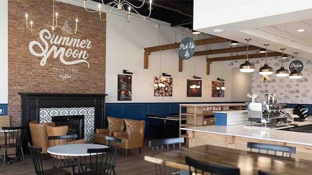 L’intérieur d’un café chaleureux, avec un mur en briques, une cheminée et un comptoir où se trouve une machine à café.