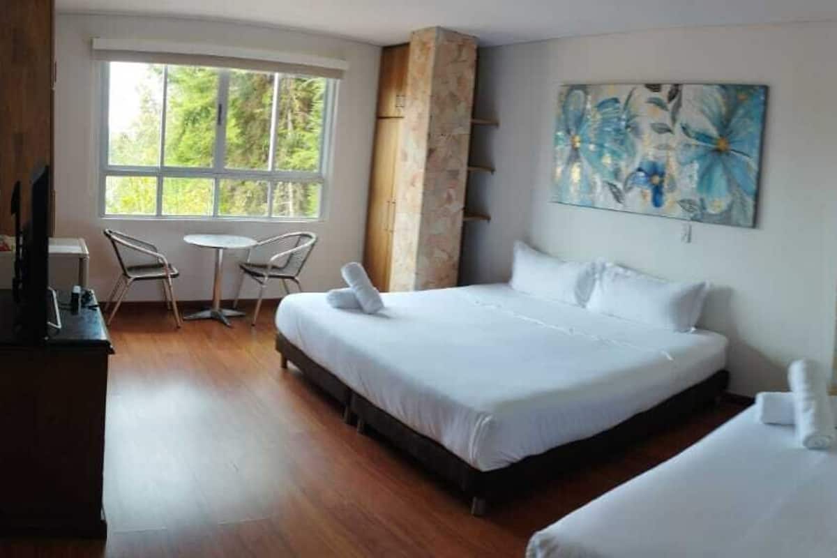 A hotel room with two beds, a desk, a chair, and a window with a view of greenery.
