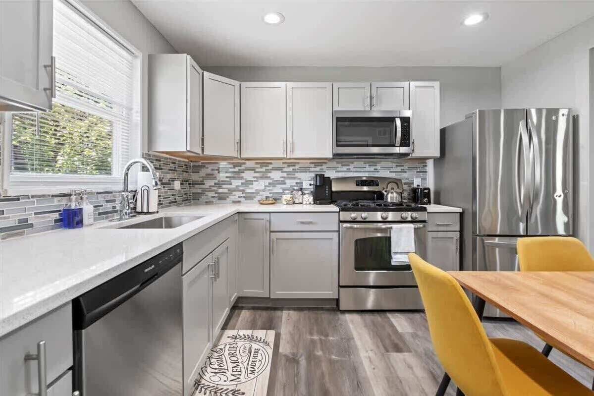 A modern kitchen with stainless steel appliances, a dishwasher, and a dining area with a yellow chair.