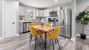A modern kitchen with white cabinets, stainless steel appliances, and a wooden dining table with yellow chairs. - Relaxing Lake Zurich 3BR + Patio | LCP Collection (Lake Zurich)