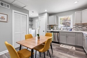 A modern kitchen with a wooden dining table and yellow chairs, grey cabinets, and a backsplash with mosaic tiles. - Relaxing Lake Zurich 3BR + Patio | LCP Collection (Lake Zurich)