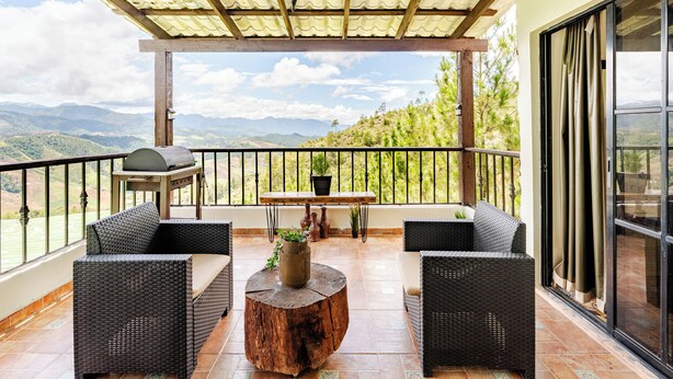 A balcony with wicker furniture, a wooden table, and a potted plant.