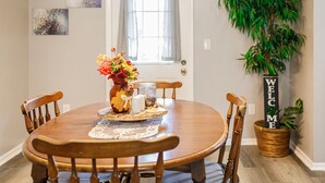 A dining area with a round wooden table, four chairs, a vase with flowers, a salt and pepper set, and a welcome sign.