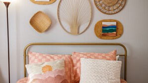 A bed with peach-patterned bedding, a gold-framed headboard, and decorative wall art including woven baskets and a framed painting.