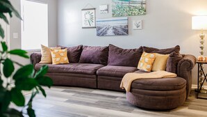 A living room with a brown sectional sofa, a side table with a lamp, and wall art.