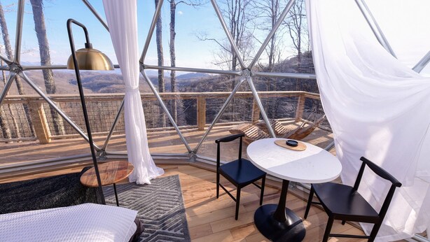 A cozy outdoor seating area with a table and chairs, a hanging lamp, and a view of the surrounding landscape.