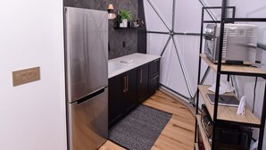 A compact kitchen with a modern design, featuring a stainless steel refrigerator, a black countertop, and a herringbone-patterned backsplash.