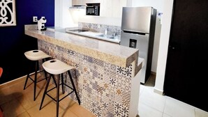 A modern kitchen with a central island, bar stools, a microwave, and a refrigerator.