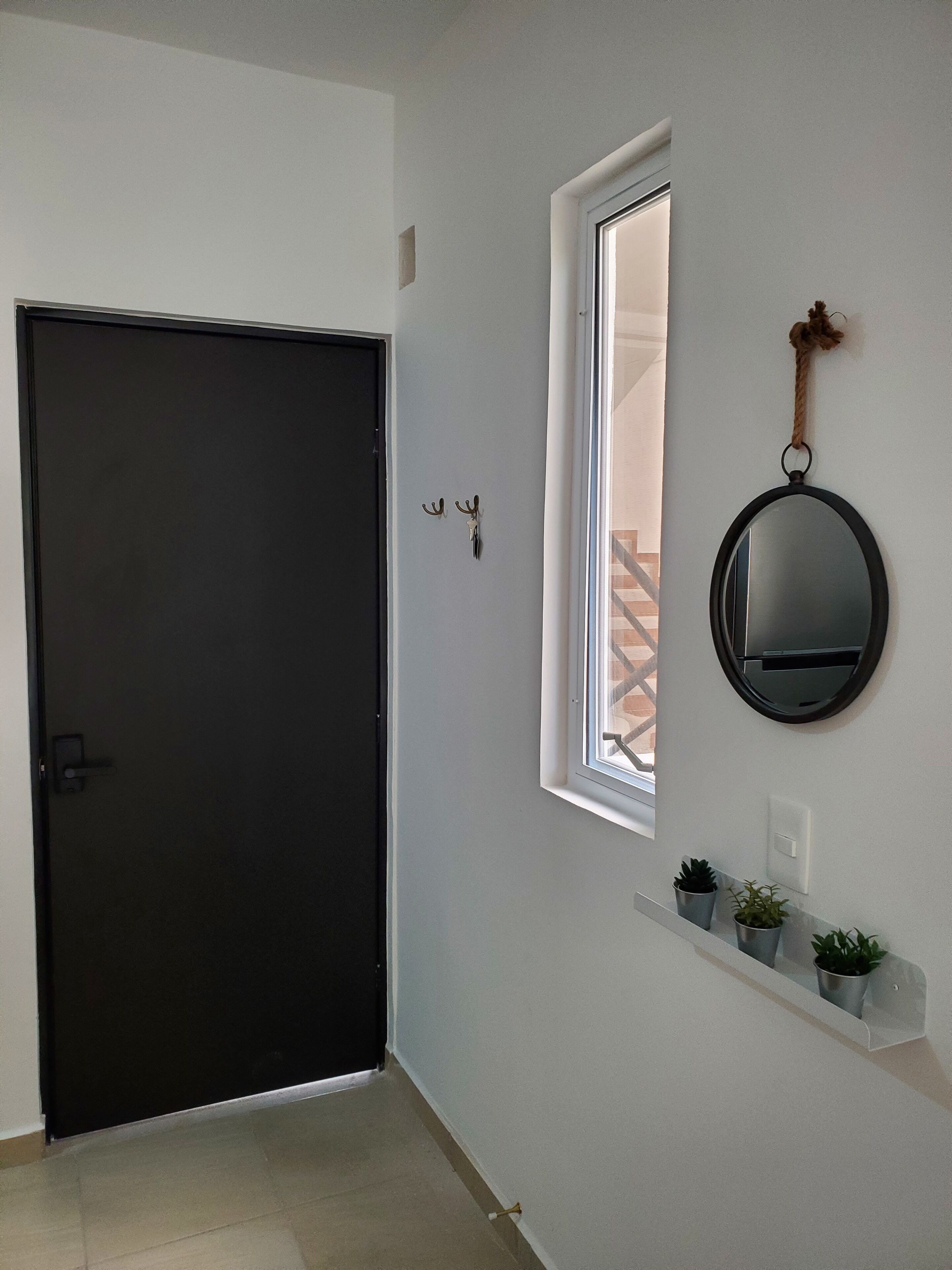 A hallway with a dark door, a window with a rope decoration, and a mirror on the wall.