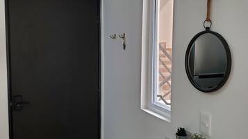 A hallway with a dark door, a window with a rope decoration, and a mirror on the wall.