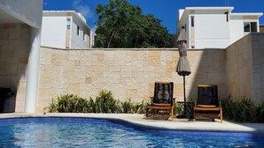 A swimming pool with two lounge chairs and a thatched roof structure.