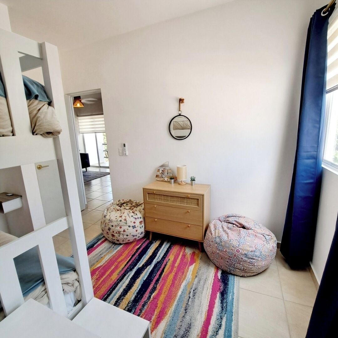 Een kamer met een gestreept tapijt, een houten dressoir, een ronde spiegel en twee zitzakken.