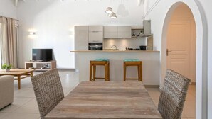 Un salon moderne avec une table à manger en bois, deux chaises, un téléviseur et un coin cuisine équipé de placards et d’un plan de travail.