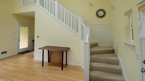 Ein geräumiger Raum mit Holzboden, einer Treppe mit weißen Geländern und einem kleinen Tisch.