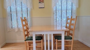 Ein Essbereich mit Holztisch und -stühlen, Spitze vor den Fenstern und einem Kalender an der Wand.
