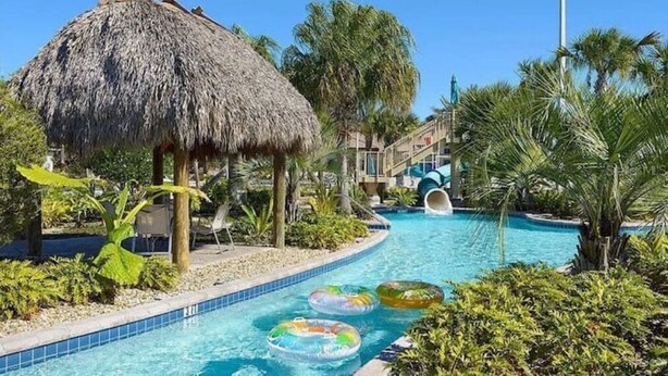 A swimming pool with a thatched-roof structure, palm trees, and inflatable rings. - Beautiful Home In Davenport, FL (Davenport)