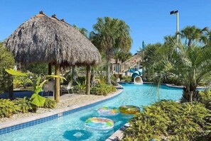 A swimming pool with a thatched-roof structure, palm trees, and inflatable rings.