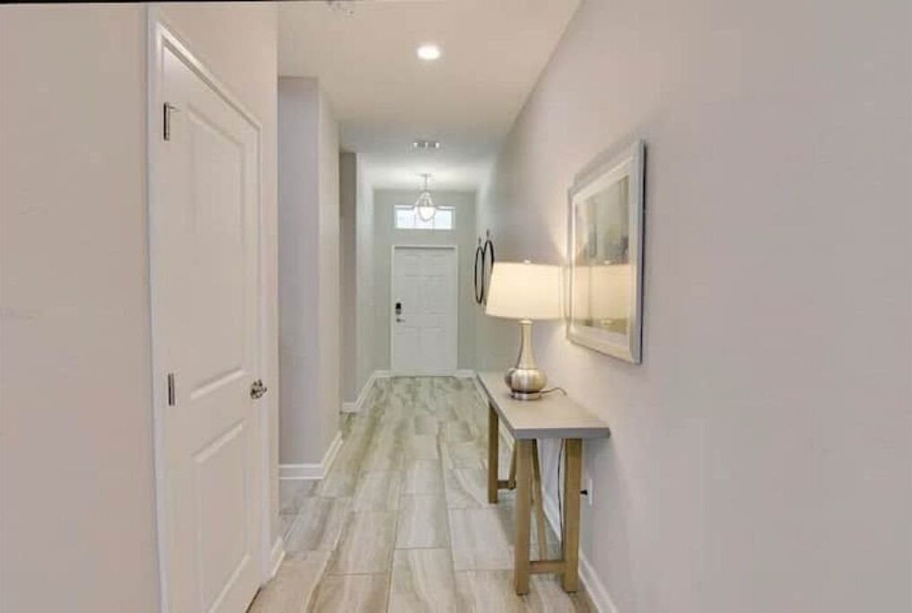 A hallway with a white door, a table with a lamp, and a framed picture on the wall.