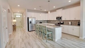 A modern kitchen with white cabinets, a granite countertop, and a central island with bar stools. - Beautiful Home In Davenport, FL (Davenport)