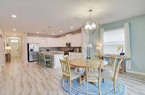 Una cocina moderna con armarios blancos, una isla central y un comedor con una mesa redonda y sillas.