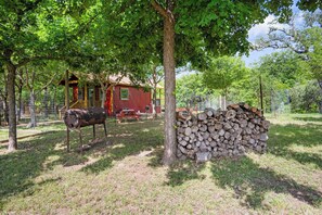 Ein eingezäunter Außenbereich mit einer Holzkonstruktion, einem Grill und einem Holzstapel.