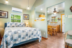 A bedroom with a bed, bedside lamps, a window with a view, and a kitchenette area with a ceiling fan. - Stronghold Red Cloud | Creekside Cabin w/ Hot Tub (Bandera)