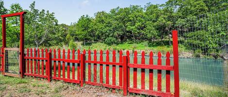 A red metal fence with a gate, surrounded by greenery and a body of water.
