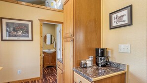A compact kitchen with wooden cabinets, a countertop, a coffee maker, and a framed picture of a duck. - Bandera Stronghold Crazy Horse (Bandera)