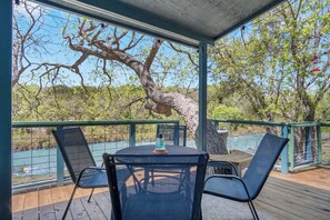 A covered outdoor area with a table and chairs, a view of a tree, and a railing.