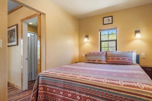 Quarto com cama, janela e porta que dá para outro espaço.