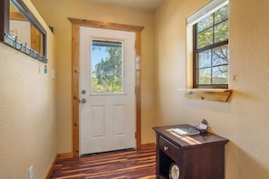 A hallway with a wooden door, a small table with a book, and a window with a view of trees.