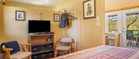 Un dormitorio con cama, televisor, armario, silla y balcón con mesa y sillas.