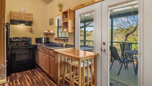 A kitchen with a built-in oven, microwave, and sink, a wooden bar area, and a view of a patio with chairs. - Bandera Stronghold Crazy Horse (Bandera)