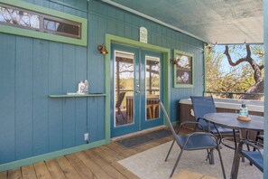 A covered outdoor seating area with a table and chairs, a door with a window, and a sign above the door. - Stronghold Crazy Horse | Cabin w/ Hot Tub & Creek (Bandera)
