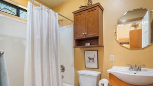 Ein Badezimmer mit Duschvorhang, Toilette, Schrank, Waschbecken und einem gerahmten Bild an der Wand.