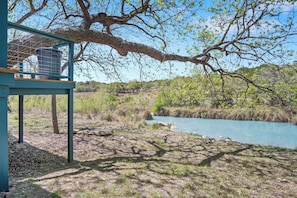 A rustic outdoor area with a wooden deck, a metal structure, and a river. - Stronghold Crazy Horse | Cabin w/ Hot Tub & Creek (Bandera)